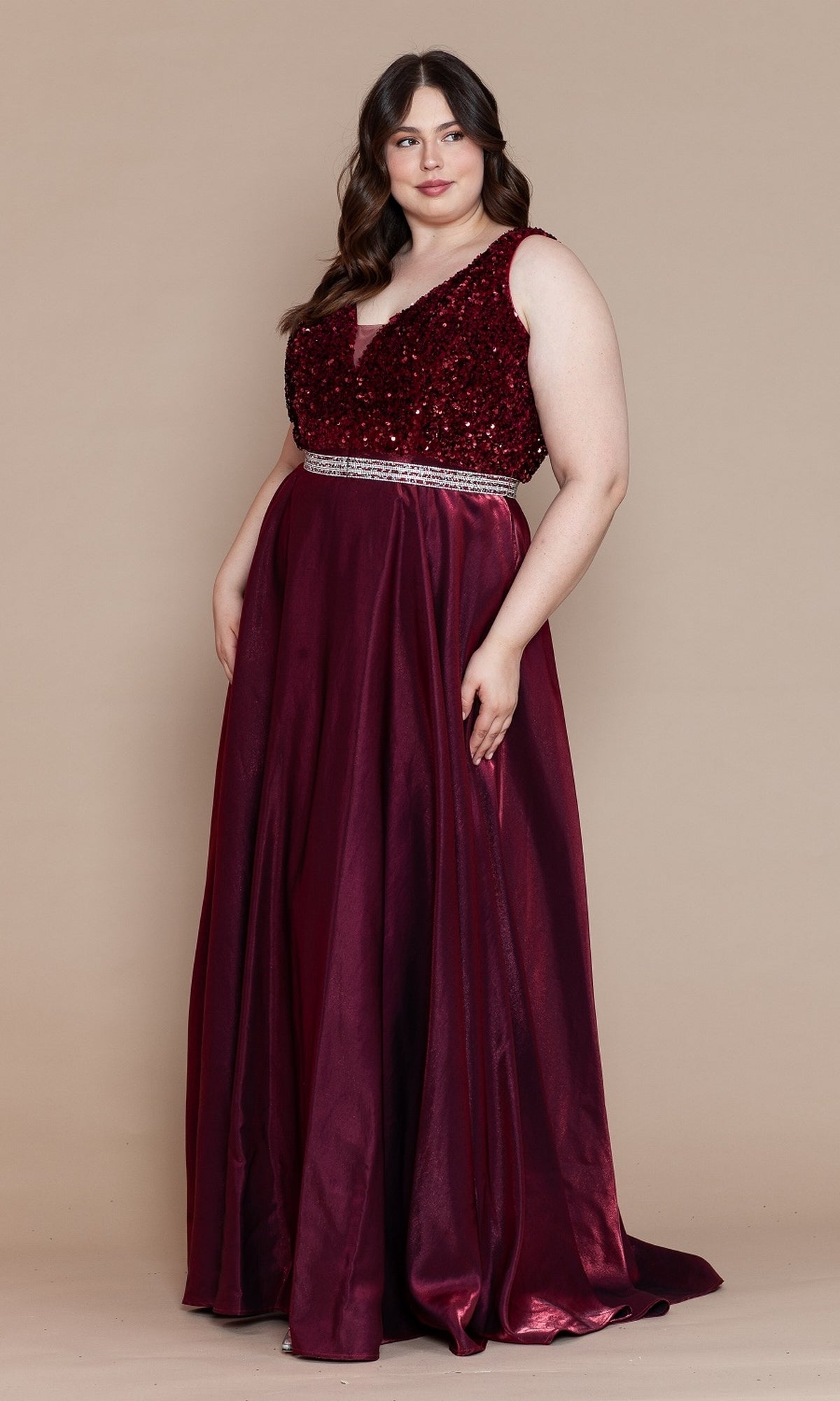A woman in the Plus-Size Long Sequin-Bodice Prom Dress W1006, a sleeveless burgundy gown with rhinestone belt, stands against a plain beige background.